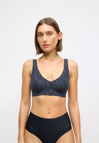 Marineblå bralette med v-udskæring og brede stropper, der har et tekstureret mønster af tynde lodrette linjer i lysere nuancer.