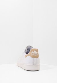 Vita lädersneakers med perforerad sidodetalj. Beige accent på hälen med "Stan Smith"-logotyp och branding. Gummisula.