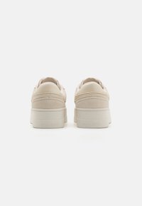 Baskets en daim beige avec une finition texturée, présentant une semelle plate et une marque "TOMMY JEANS" à l'arrière. Bout rond et col rembourré.