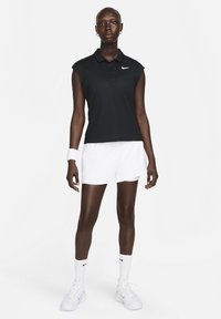 Black sleeveless polo shirt with a collar, featuring a white Nike logo. Paired with white athletic shorts and white socks, worn with white sneakers.