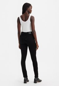 Zwarte skinny jeans met een hoge taille, gecombineerd met een witte tanktop. De jeans hebben achterzakken en een logo-opdruk op de tailleband.