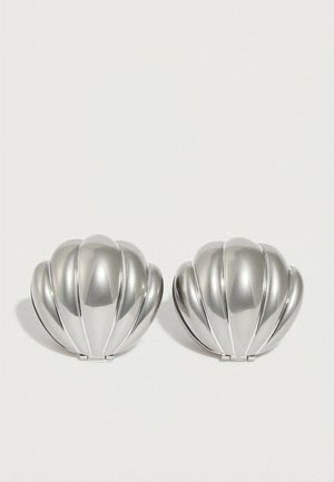 Dva kompaktna ogledala u srebrnoj boji u obliku školjke s rebrastim detaljima, postavljena jedan pored drugog na bijeloj pozadini.