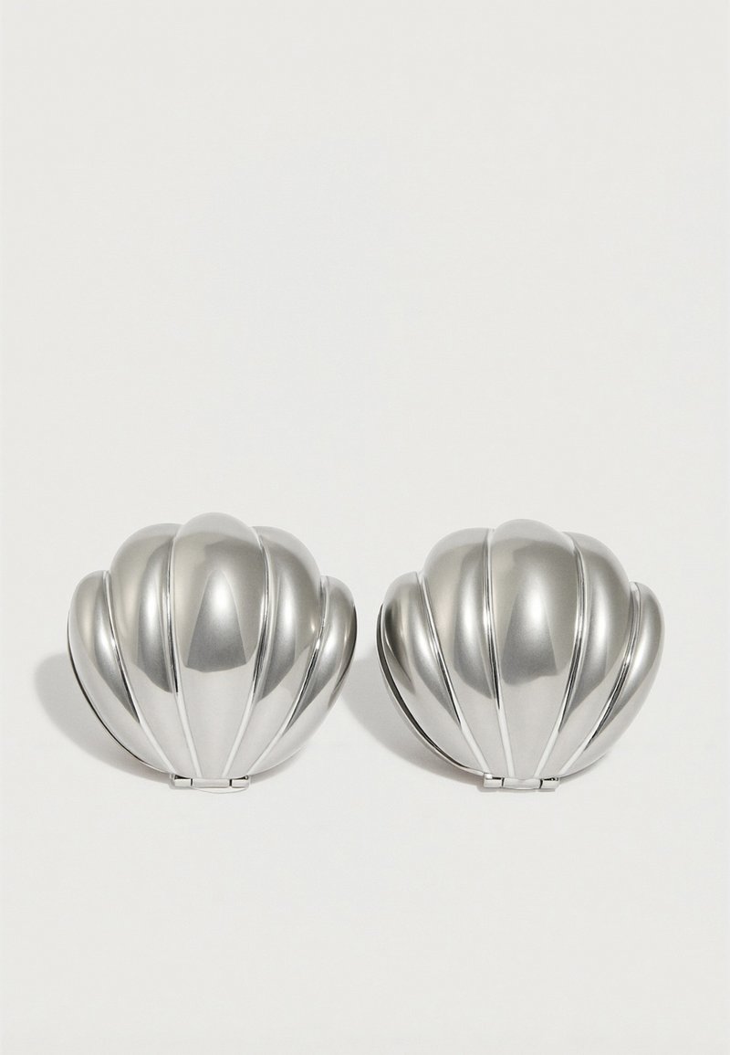 Δύο συμπαγείς καθρέφτες σε σχήμα κοχυλιού με ασημένιο τόνο και ραβδώσεις, τοποθετημένοι δίπλα-δίπλα σε λευκό φόντο.