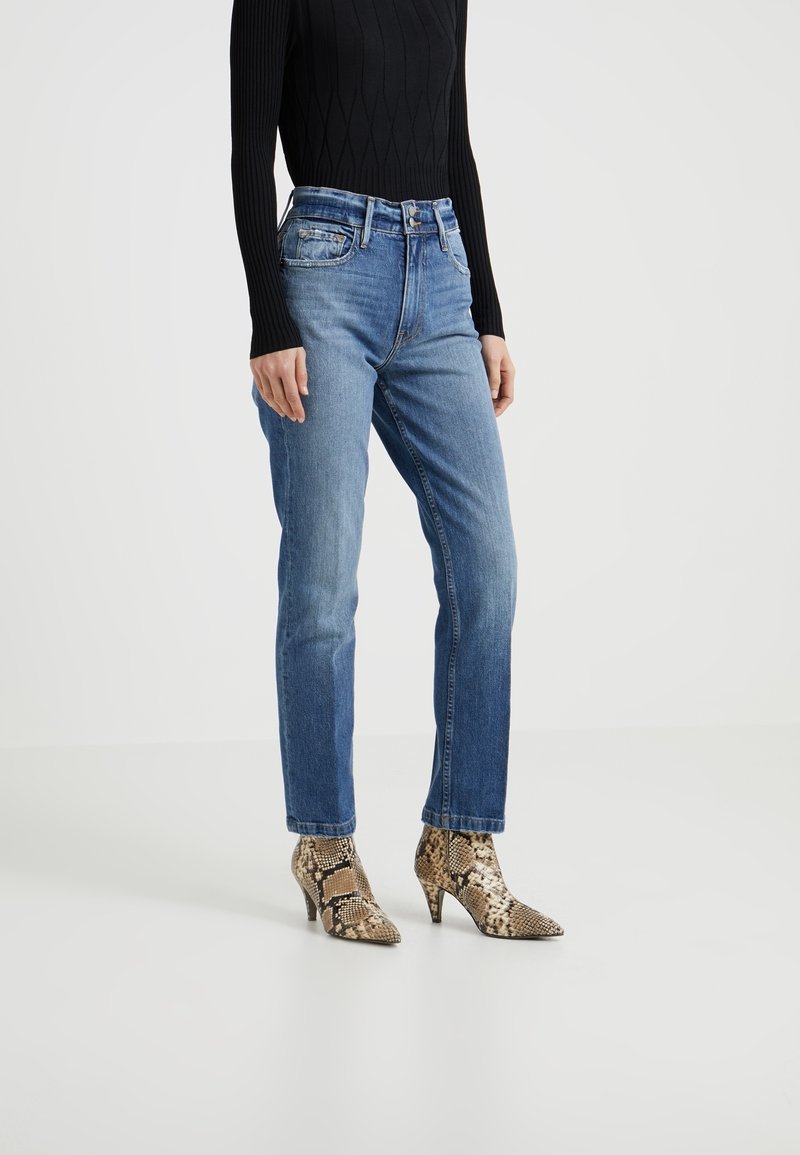 Blå raka jeans i denim, kombinerade med en svart ribbad långärmad topp och spetsiga klackar med ormskinsmönster.