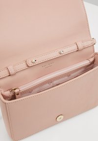 Borsa a tracolla in pelle rosa chiaro con texture liscia, tasca interna con zip e dettagli in hardware dorato. Presenta il logo del brand impresso all'interno.