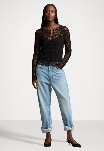 Black lace long-sleeve top with floral patterns and scalloped edges, paired with light blue rolled-up baggy jeans and black heeled shoes.