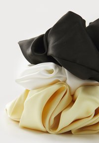 Silk scrunchie in black, white, and yellow. Features soft, shiny texture with gathered fabric, creating a voluminous, elegant shape.