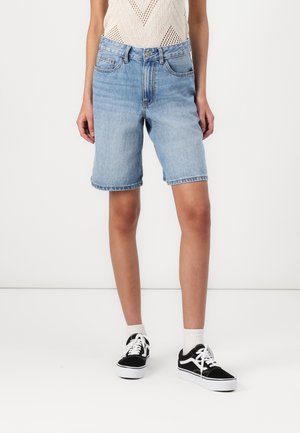 Shorts en denim bleu clair à coupe droite, dotés de cinq poches et d'ourlets effilochés, associés à des baskets noires et blanches.