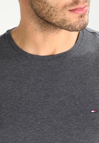 Grå rundhalset T-shirt lavet af bomuldsblanding, med et lille logo på venstre brystområde. Glat tekstur, tætsiddende design.
