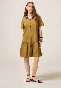 Rochie cu mânecă scurtă și guler închis, de culoare verde măslin, cu fustă plisată. Material ușor, croi lejer și asortată cu sandale negre.