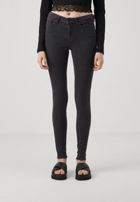 Jeans negros ajustados con una textura suave, que cuentan con un diseño clásico de cinco bolsillos y una cintura de altura media, combinados con sandalias negras tipo slider.