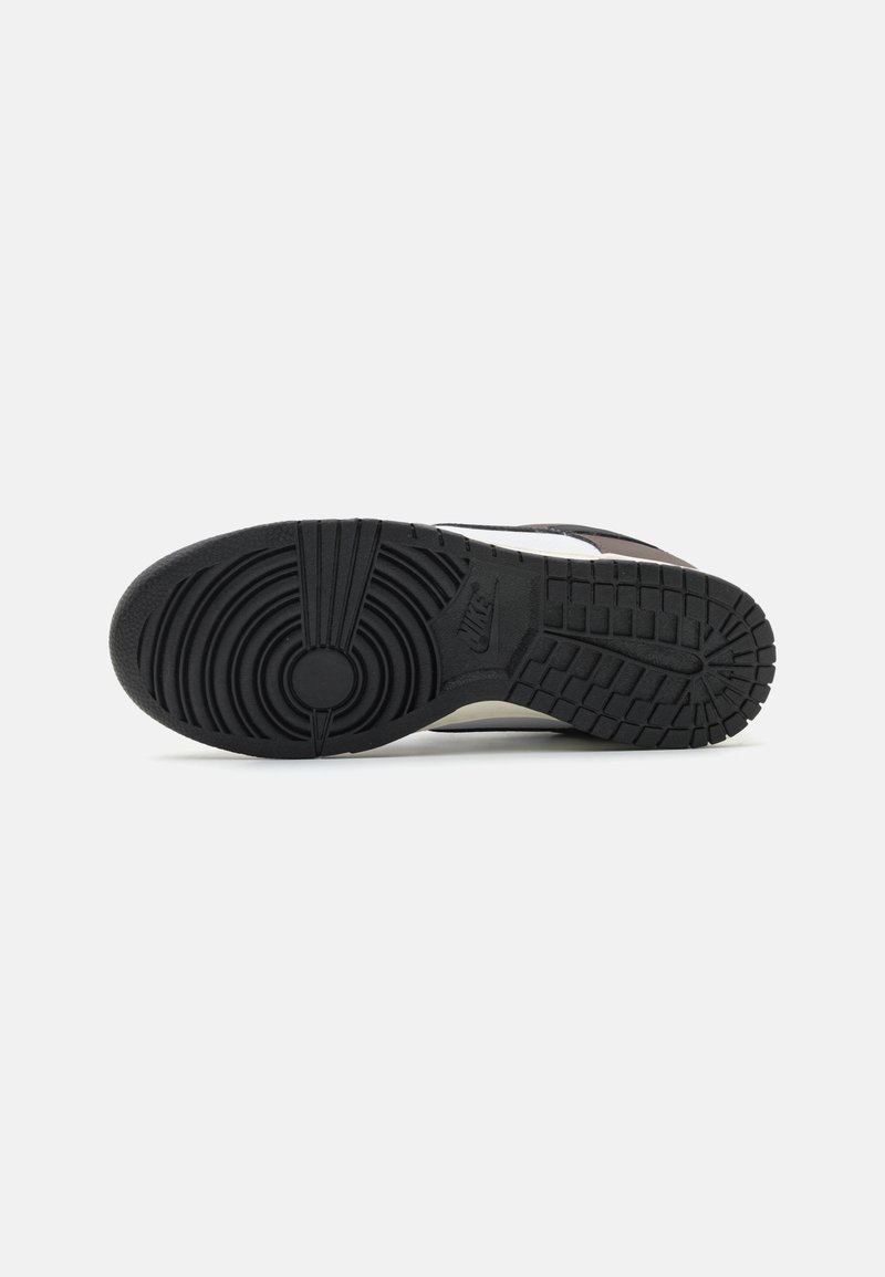 Semelle de sneaker Nike, en caoutchouc noir avec un motif de bande de roulement texturé, élément central circulaire et accents blancs le long du bord.