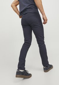 Vaqueros ajustados de color azul marino con una textura suave, que cuentan con bolsillos traseros y un par de zapatillas oscuras con suelas de goma marrón.