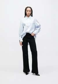 Light blue striped shirt with a collar, paired with black flared trousers. The outfit features a relaxed fit and smooth fabric texture.