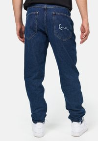 Μπλε τζιν παντελόνι με χαλαρή εφαρμογή, πίσω τσέπες και λευκή κεντημένη διακόσμηση στη δεξιά τσέπη. Φοριέται με λευκά αθλητικά παπούτσια.