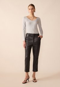 Top de manga larga gris combinado con pantalones de cuero negros recortados que presentan costuras frontales, bolsillos laterales y sandalias de tacón alto con tiras.