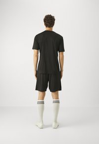 Svarte treningsdrakt med kortermet genser og shorts, med en avslappet passform, kombinert med hvite knehøye sokker med svarte striper og fotballstøvler.