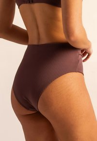 Parte inferior de bikini de talle alto en un color malva profundo, con textura acanalada y acabado suave, que presenta un diseño sin costuras y una cinturilla elástica.