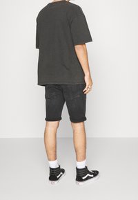 Camiseta negra de gran tamaño, pantalones cortos de mezclilla negros y zapatillas altas negras con detalles en blanco. El conjunto incluye pantalones cortos con dobladillo enrollado y calcetines de contraste.