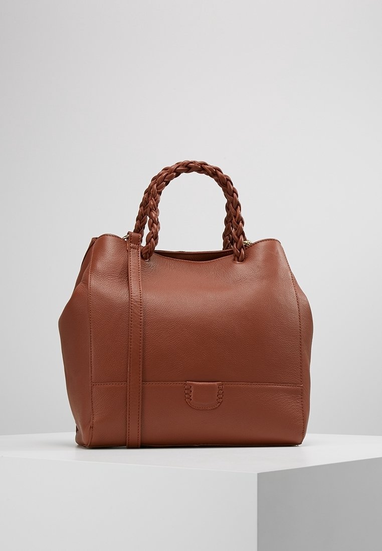 Bruine leren handtas met een gestructureerde afwerking, voorzien van gevlochten handvatten en een afneembare schouderriem. Rondvormig met subtiele details aan de voorkant.