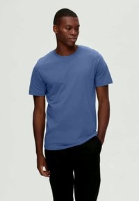 Μπλε βαμβακερό t-shirt με στρογγυλή λαιμόκοψη και κοντά μανίκια, φορεμένο με απλά μαύρα παντελόνια. Λείο υφή, απλός σχεδιασμός.