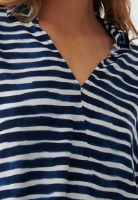 Blusa con scollo a V caratterizzata da strisce verticali blu navy e bianche, realizzata in tessuto leggero con una texture liscia. Design con colletto e cuciture sottili.