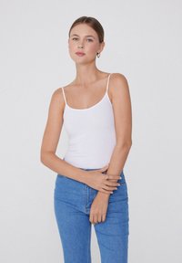 Bílý žebrovaný top na tenkých ramínkách, spárovaný s modrými džínami s vysokým pasem. Jednoduchý design, hladká textura a přiléhavý střih.