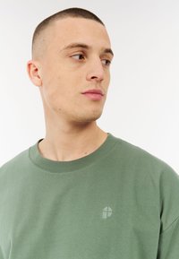 Groene katoenen sweatshirt met een ronde hals, met een subtiele logo in een lichtere tint. Zachte textuur en een ontspannen pasvorm.