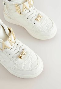 Hvide høje sneakers med quiltet tekstur, guld "BAK" accent og sløjfedetail på snørerne. Gummisål for godt greb og holdbarhed.