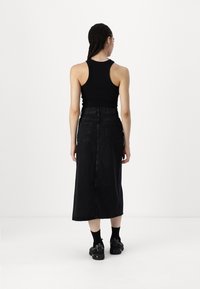 Saia de ganga preta com cintura alta, bolsos traseiros e design reto. Combinada com um top de alças preto e sapatos grossos pretos.