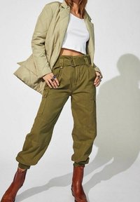 Olivgrön cargobyxor med hög midja och bälte, tillsammans med en vit croptop och en ljusbeige vadderad jacka. Bruna ankelstövlar.