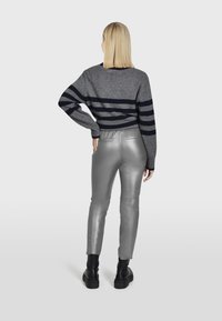 Šedý sveter s námorníckymi pruhmi, kombinovaný s lesklými striebornými nohavicami. Outfit má dlhé rukávy a nohavice so zúženým strihom po členky. Čierne topánky.