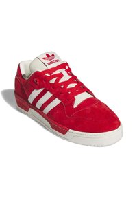 Zapatillas de ante rojo con acentos de cuero blanco, que cuentan con tres rayas blancas, una lengua acolchada y suela de goma Texturizada.