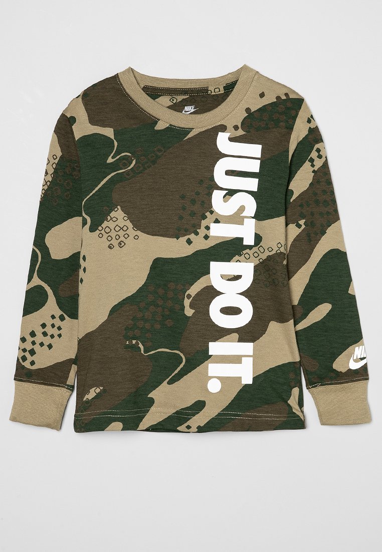 Chemise camouflage à manches longues avec "JUST DO IT." en lettres blanches en gras de manière verticale sur le devant et un petit logo Nike blanc sur le poignet gauche.