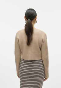 Bež pulover s rebrasto teksturo, kratek kroj in dolgi rokavi, v kombinaciji s sivo črtasto midi krilo. Strukturirano pleteno blago prikazano zadaj.