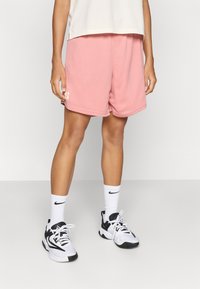 Ροζ αθλητικό σορτς από διχτυωτό ύφασμα με ελαστική μέση και πλαϊνές τσέπες. Συνδυασμένο με λευκές κάλτσες και  μαύρα αθλητικά παπούτσια.