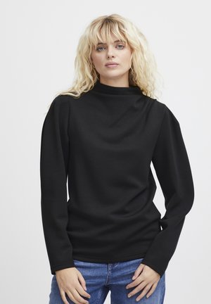Schwarzes Langarmoberteil mit hohem Kragen, glatter Textur und leicht gepufften Schultern, kombiniert mit hellblauen Jeans.
