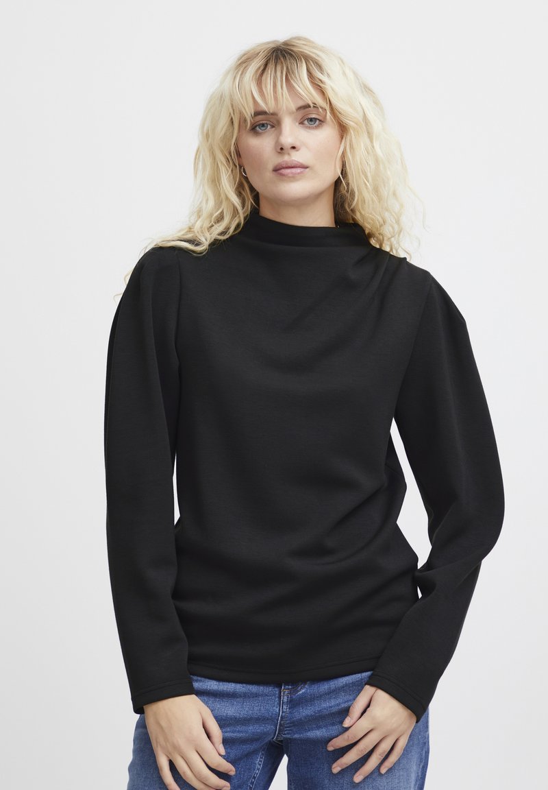 Maglietta nera a maniche lunghe con collo alto, texture liscia e spalle leggermente a sbuffo, abbinata a jeans azzurri chiari.