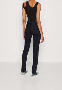 Černý bezrukávový body oblečený s tmavě modrými skinny džíny s vysokým pasem. Outfit doplňují zelené a bílé kostičkované slip-on boty.