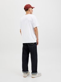 Valge lühikeste varrukatega t-särk, tume sinine teksapüksid üleskeeratud käistega ja heleda värvusega tossud. Müts on punane, vaadatuna tagant. Lihtne disain.