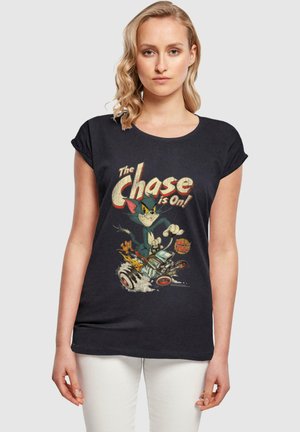 Schwarzes T-Shirt mit kurzen Ärmeln, das einen Vintage-Cartoon mit einer Katze und einer Maus in einem Auto zeigt, mit dem Text "Die Verfolgung läuft!" in Fettschrift.