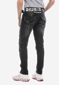 Zwarte skinny jeans met studs op de achterzakken, leren details en een contrasterende witte tailleband. Heeft een slim fit en een vervaagd textuur.