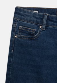 Tmavě modré džíny mají klasický pětikapsový design, s viditelným šitím a malou přední kapsou. Textura je hladká a odolná.