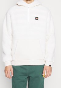 Krämfärgad fleece-hoodie med halvmidja, framficka och elastiska ärmslut. Har en liten logotyp på bröstet och en texturerad yta.