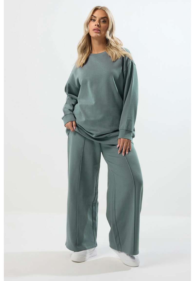 Ljusgrön oversized sweatshirt och vida byxor i mjukt tyg med ribbade manschetter, tillsammans med vita sneakers. Enkelt design och avslappnad passform.