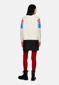 Knit sweater with white body, striped blue and red sleeves; paired with a black quilted skirt, red tights, and black boots.