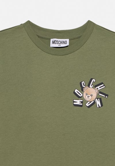 Camiseta para niños de color verde oliva con cuello redondo acanalado y un dibujo de un osito rodeado de letras "MOSCHINO" dispersas en el pecho.