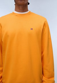 Orange sweatshirt lavet af blødt materiale, med ribbet rund hals og et lille broderet norsk flag på venstre bryst.