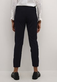 Navy slacks with a tailored fit, featuring a smooth texture and two back pockets. Paired with black footwear and a white shirt.