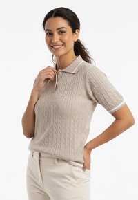 Beżowa dzianinowa koszulka polo z teksturowanym wzorem warkocza, z kołnierzykiem i krótkimi rękawami ozdobionymi białymi paskami.